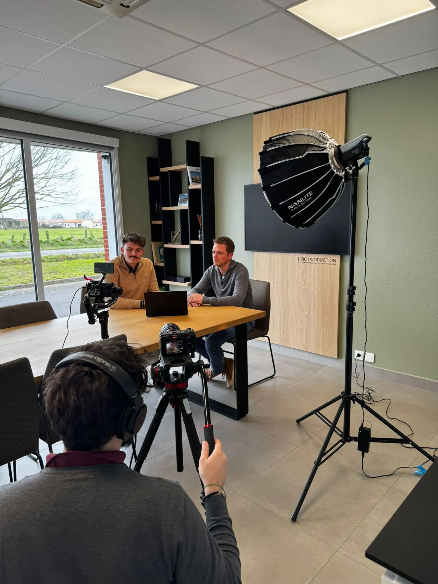 Tournage d’une interview à deux voix dans une salle de réunion, caméra sur trépied et boîte à lumière.